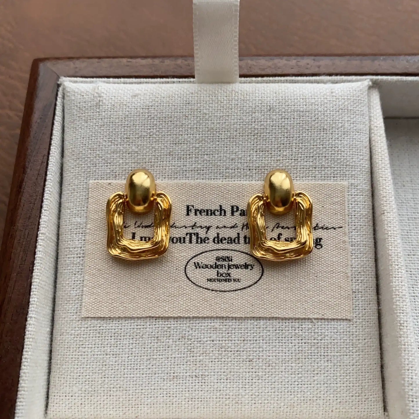 Gold molten metal geometric square stud earrings displayed on linen jewelry box