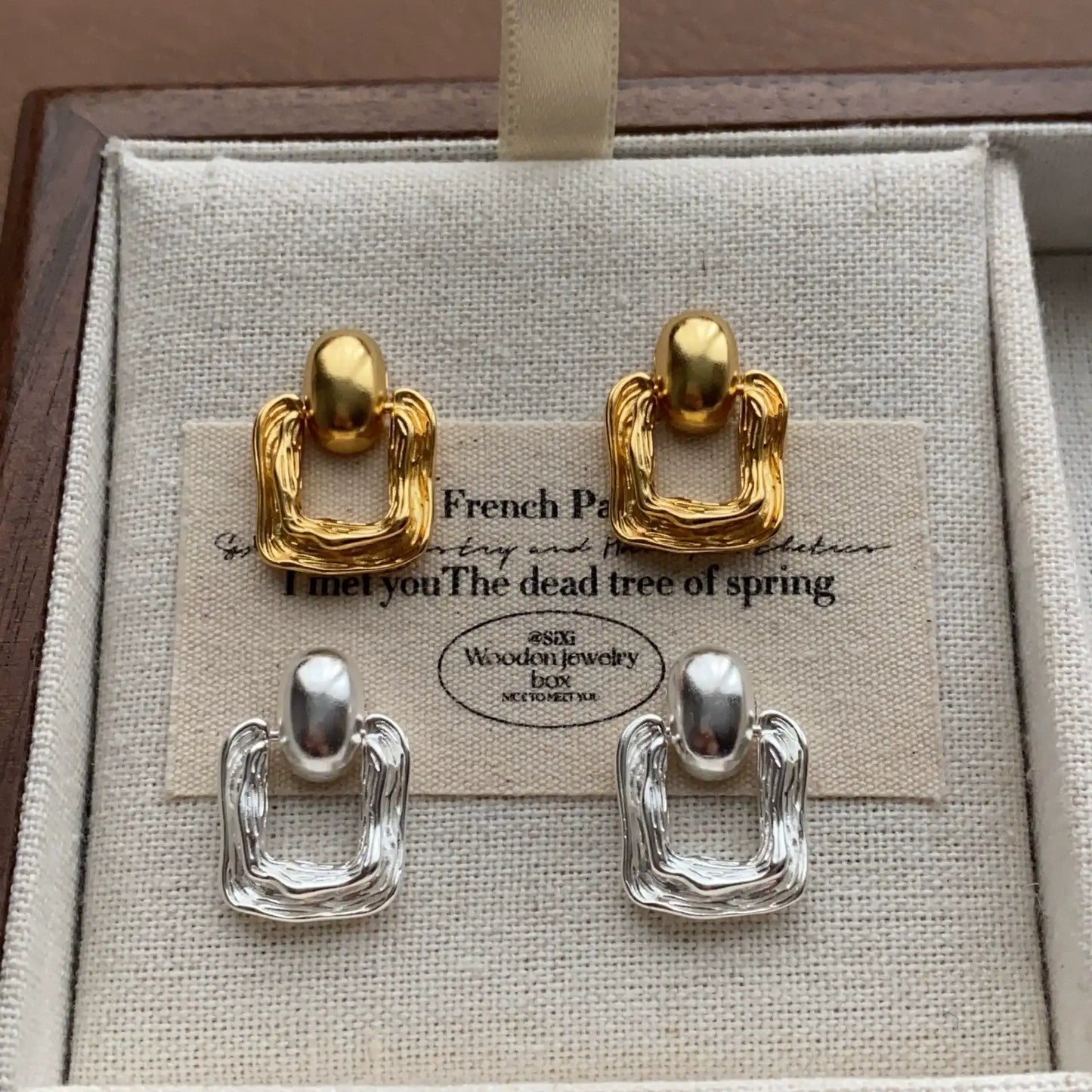Gold and silver geometric square stud earrings shown together on linen display