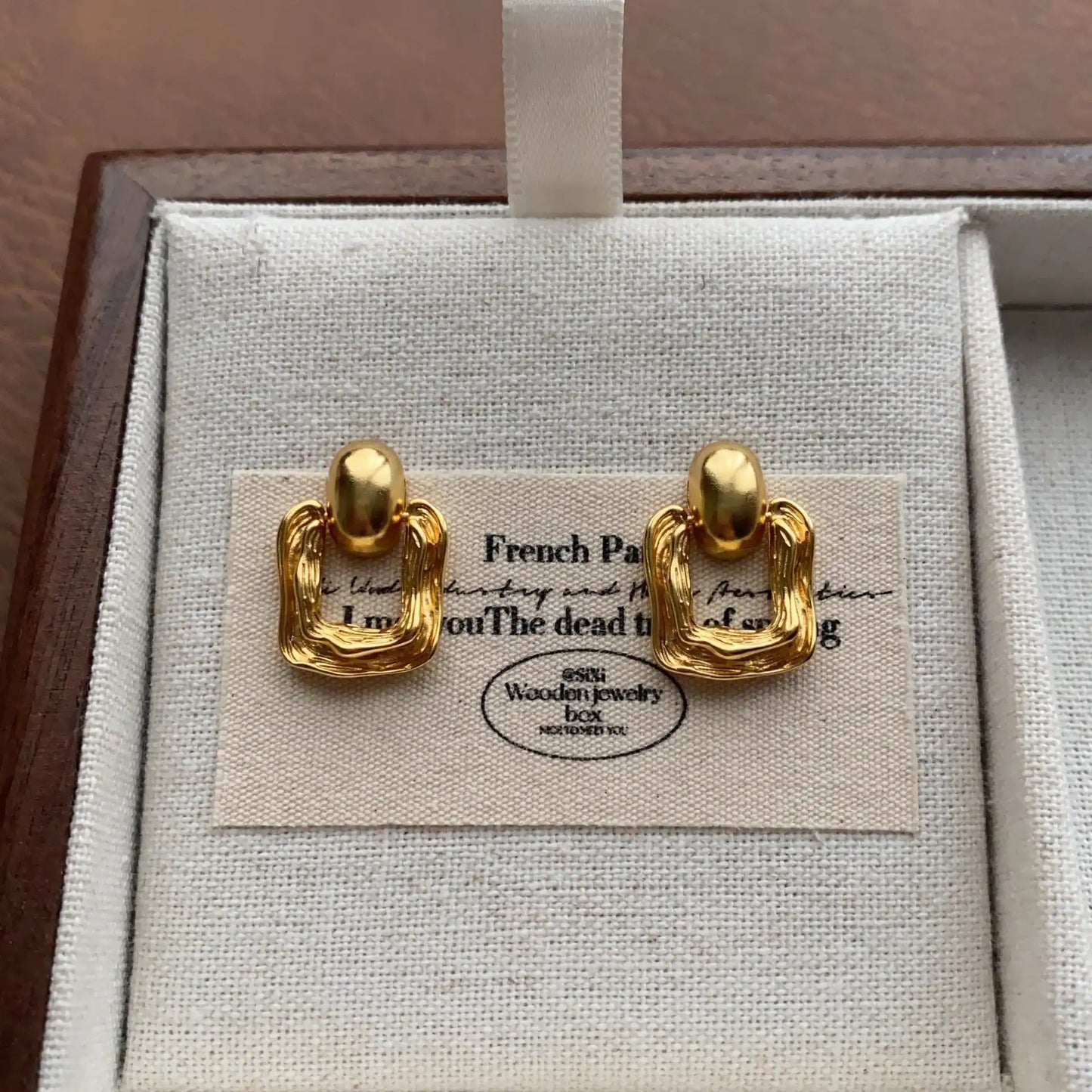 Close-up of gold textured square stud earrings with modern organic shape
