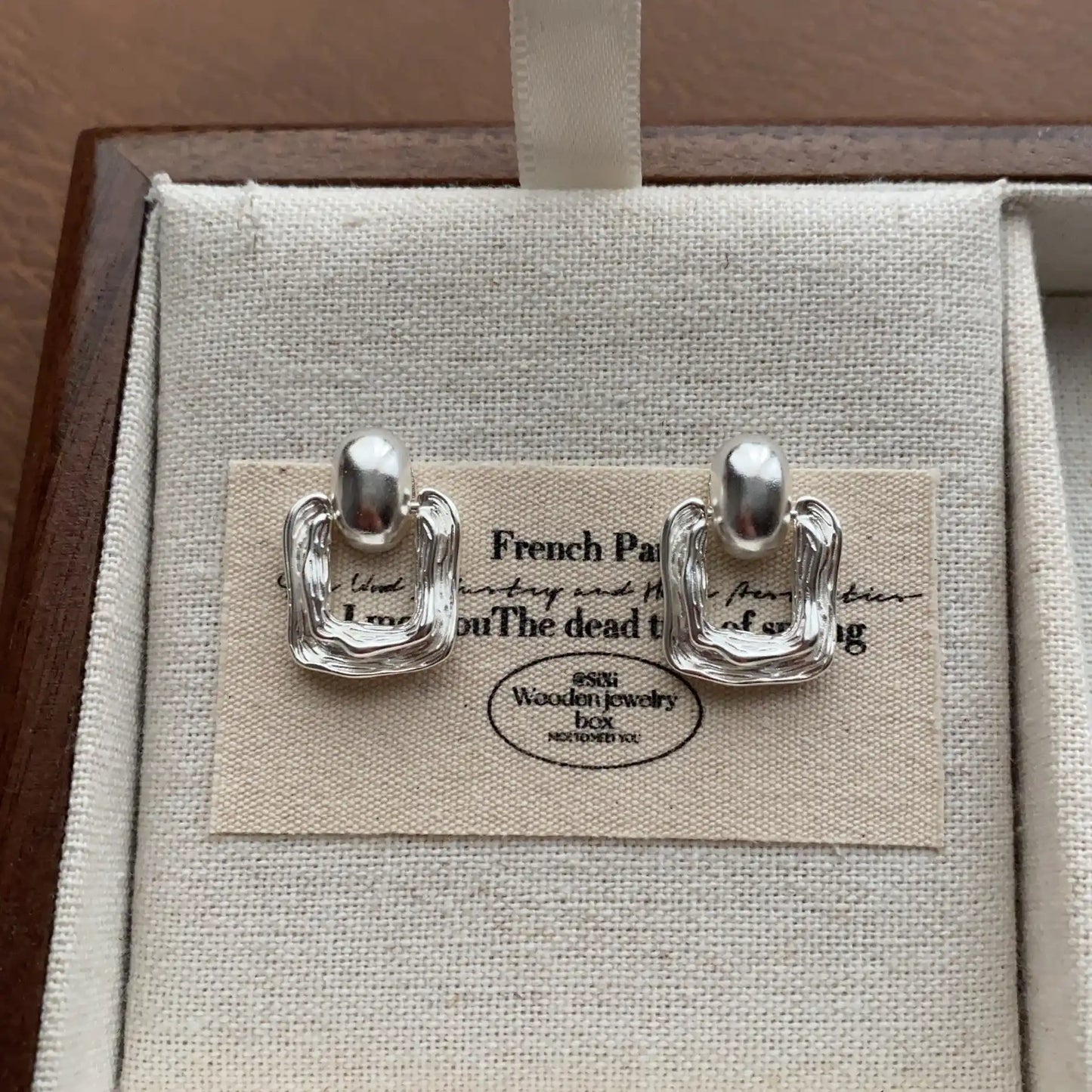 Close-up of silver irregular metal square stud earrings on neutral jewelry box