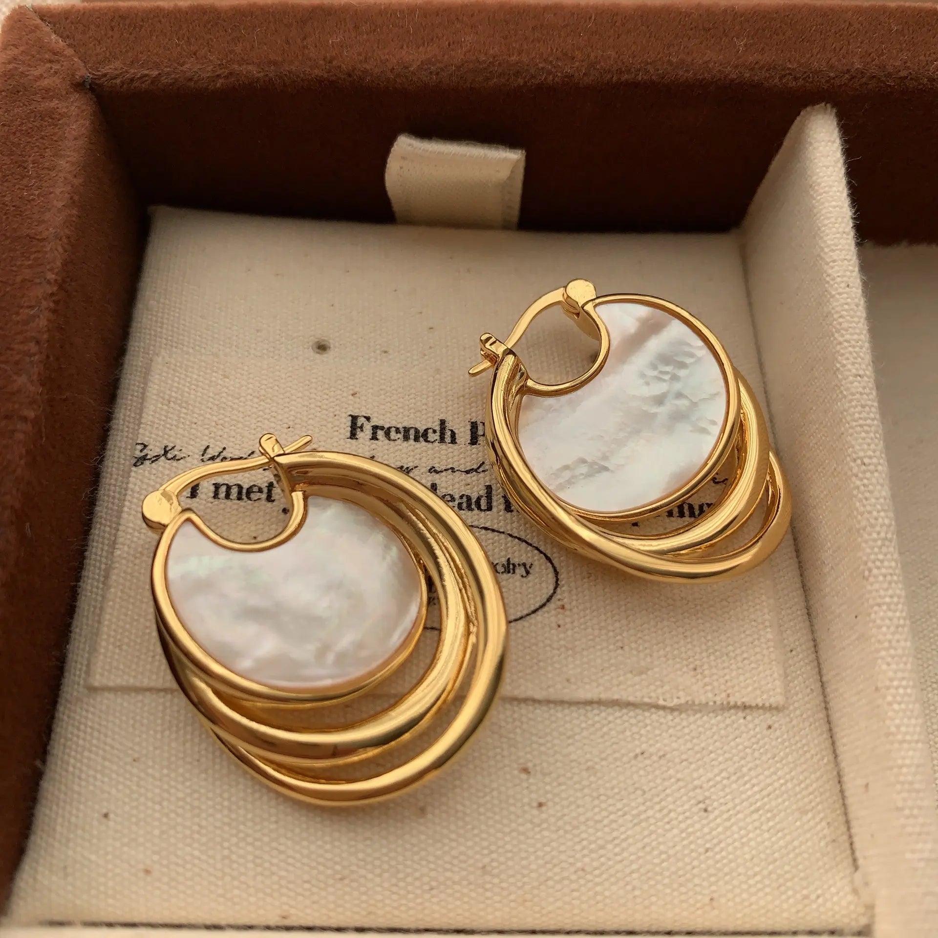 Mother of pearl disc earrings with layered gold hoops displayed in a velvet jewelry box