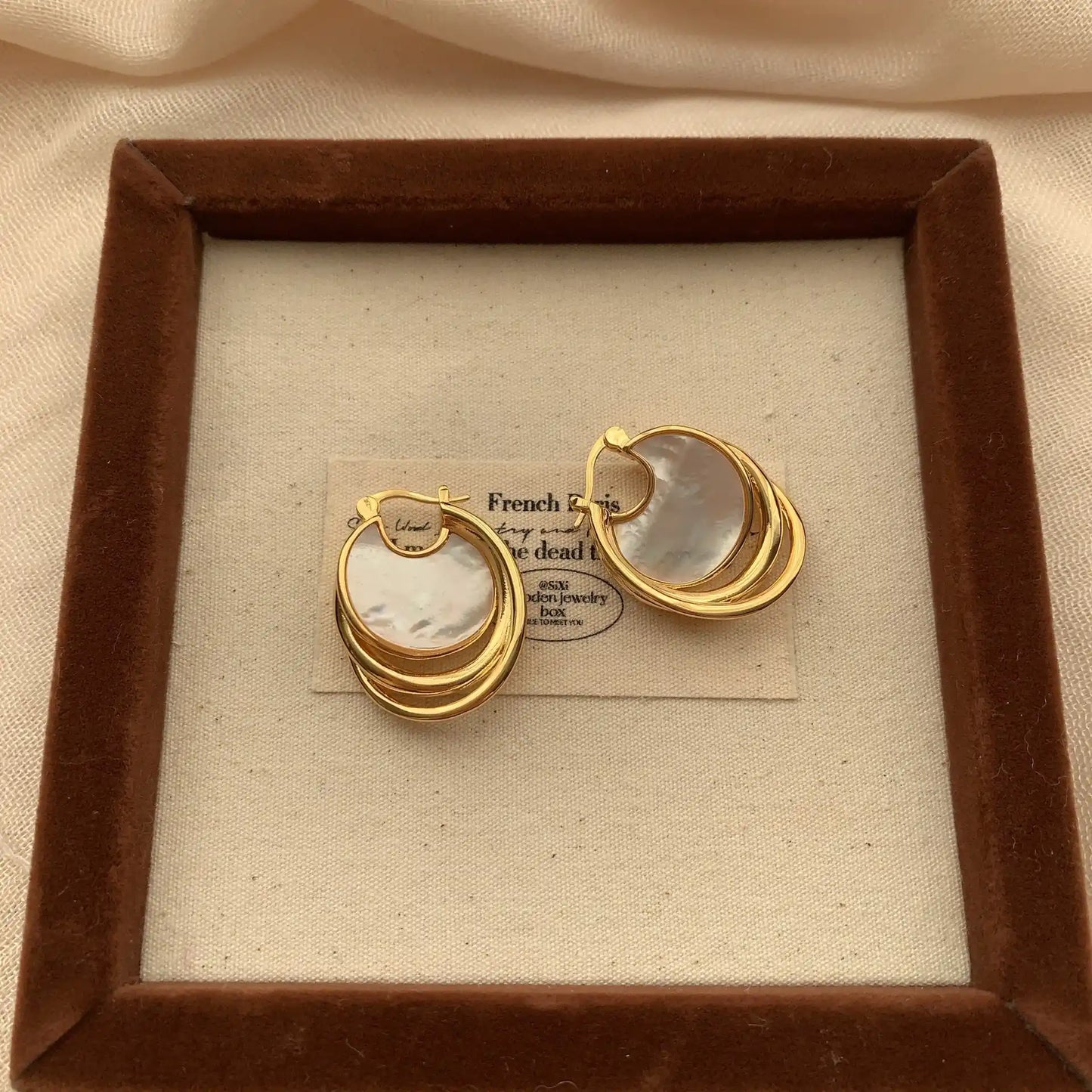 Pair of natural shell disc earrings with interlocking gold hoops on a square jewelry display