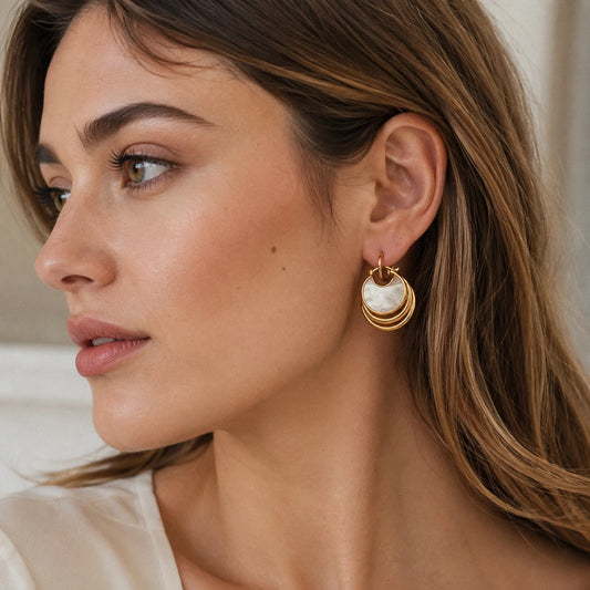 Model wearing mother of pearl disc earrings with layered gold hoops and an elegant neutral outfit