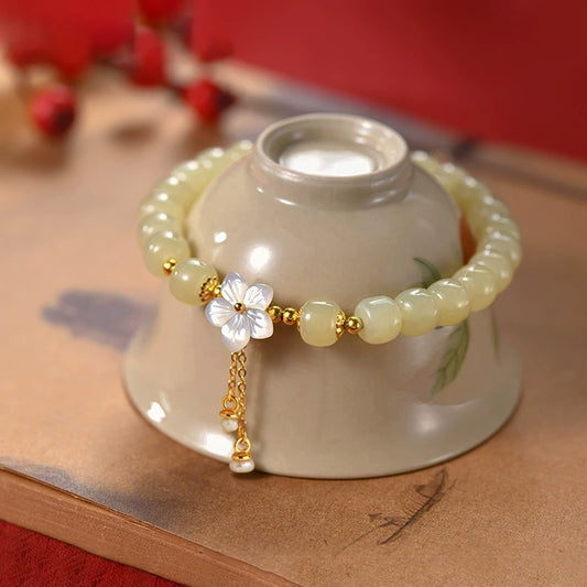 Hetian jade sakura bracelet with freshwater pearl tassel styled on ceramic cup.
