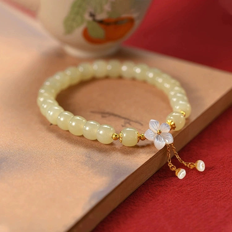 Pale green nephrite jade bracelet with mother of pearl flower charm on book.