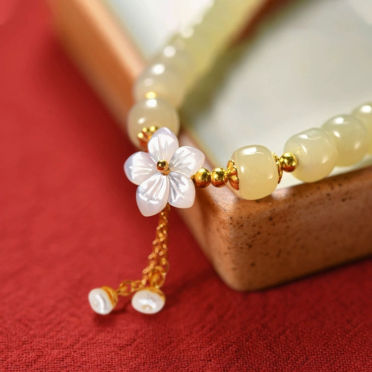 Close-up of Hetian jade bracelet with shell sakura charm, S925 accents, and pearl tassel.