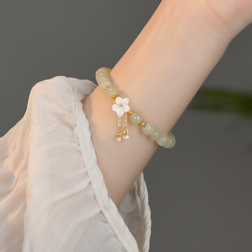 Dainty Hetian jade flower bracelet with freshwater pearl tassel on wrist.