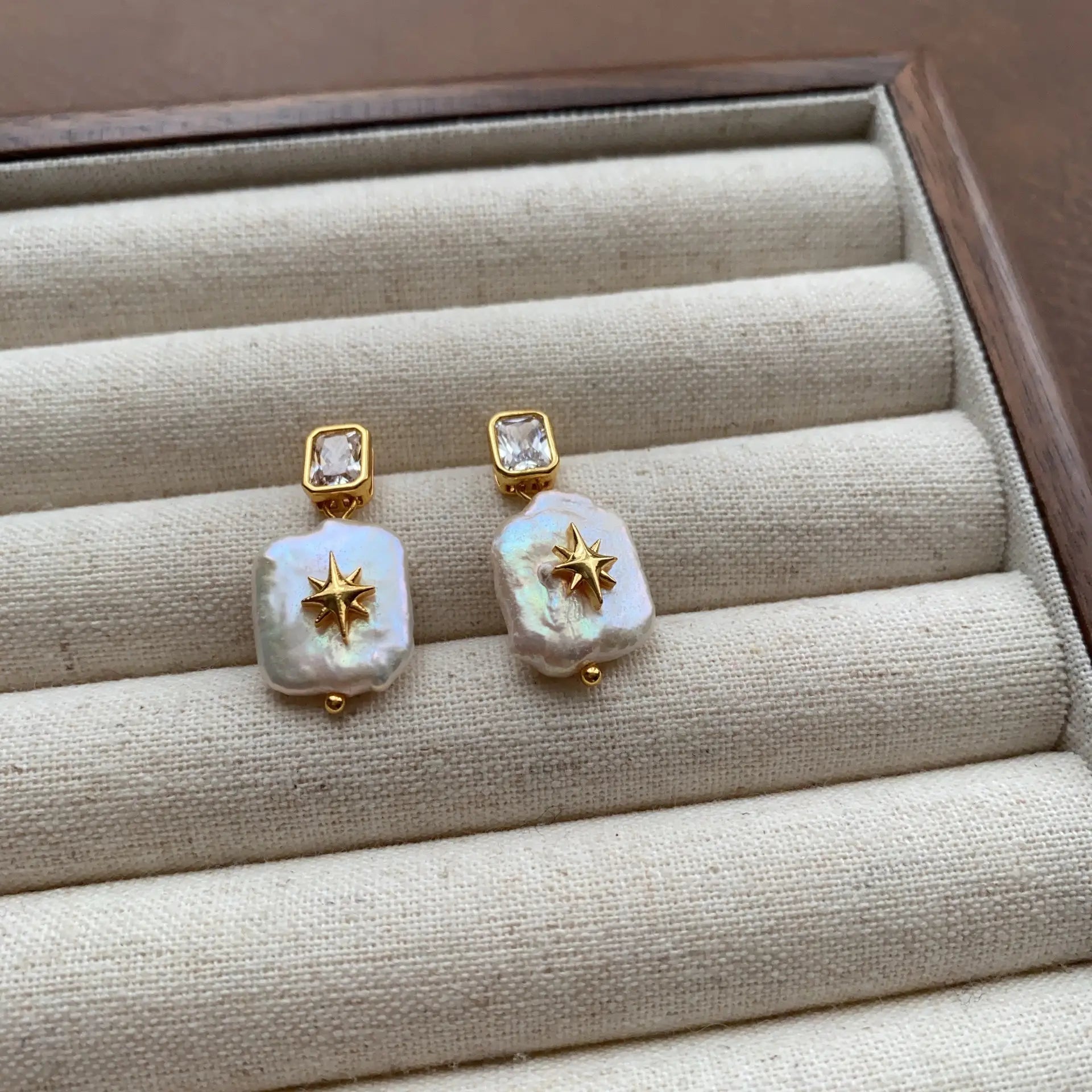 North Star baroque pearl earrings with rectangular crystal studs arranged on a linen jewelry tray