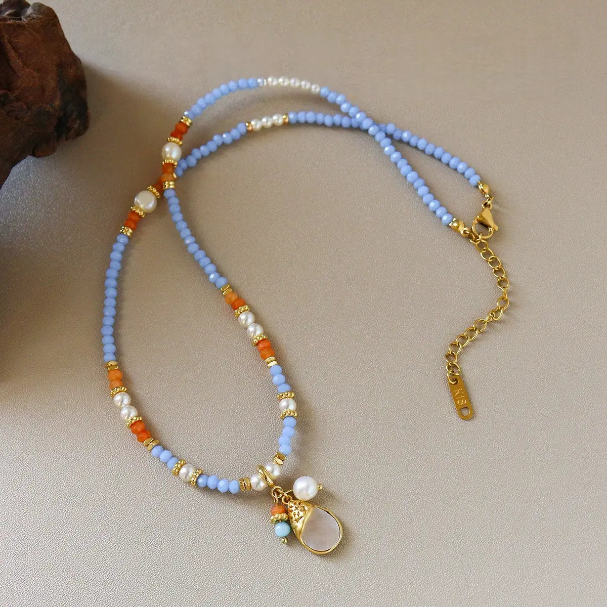 Pastel blue shell teardrop pendant necklace with glass beads, natural stone, brass details, and pearl accents