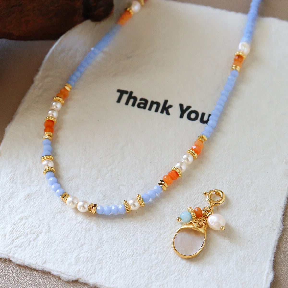 Pastel blue glass bead necklace with shell teardrop pendant and pearl accents displayed on gift pouch