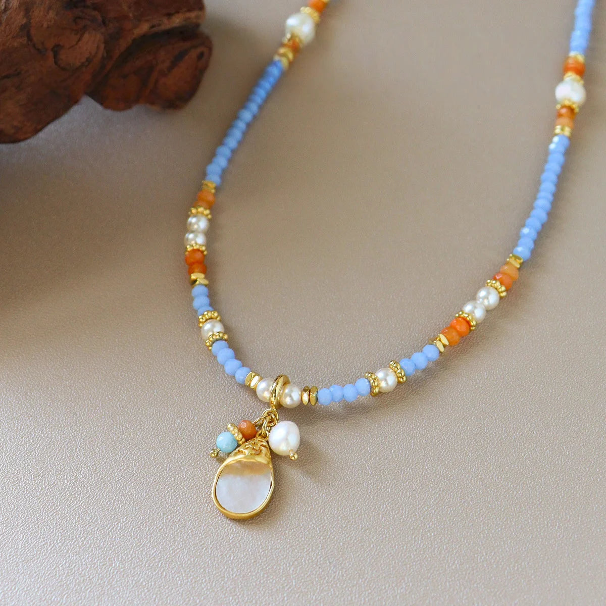 Close-up of pastel blue shell pendant necklace with orange glass beads, pearl details, and brass accents