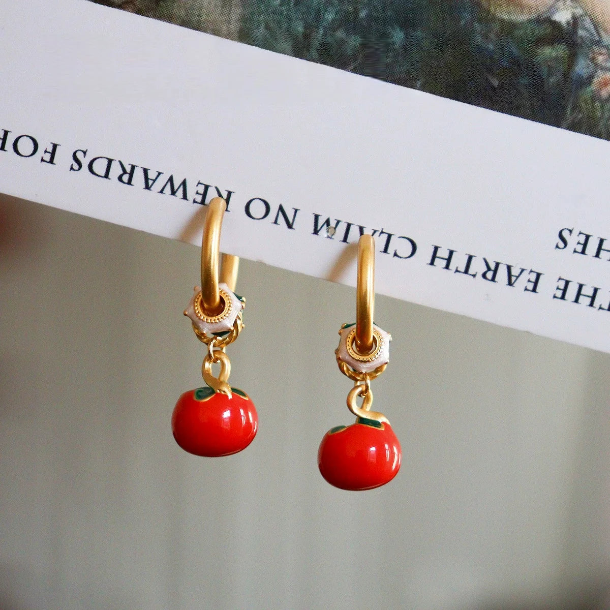 Red persimmon dangle earrings hanging from polished gold tone brass hoops