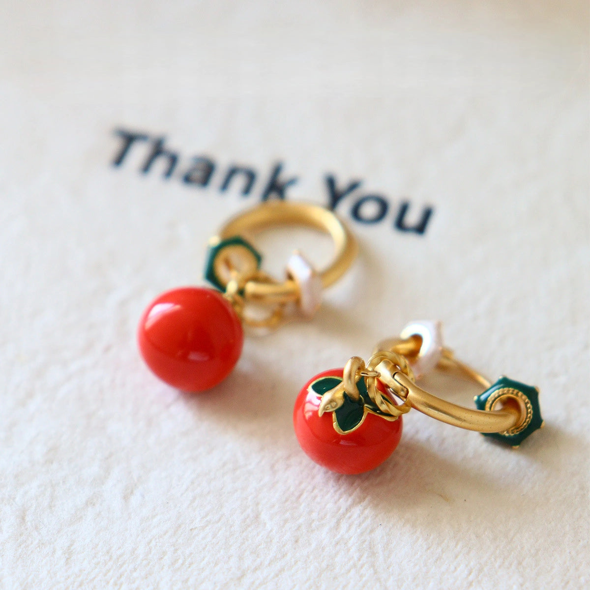 Close-up of red persimmon earrings with glossy fruit drops and decorative green accents