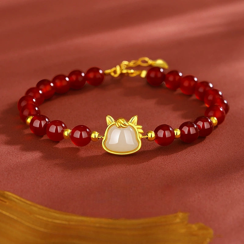 Red agate beaded bracelet with white jade horse accent on warm red satin.