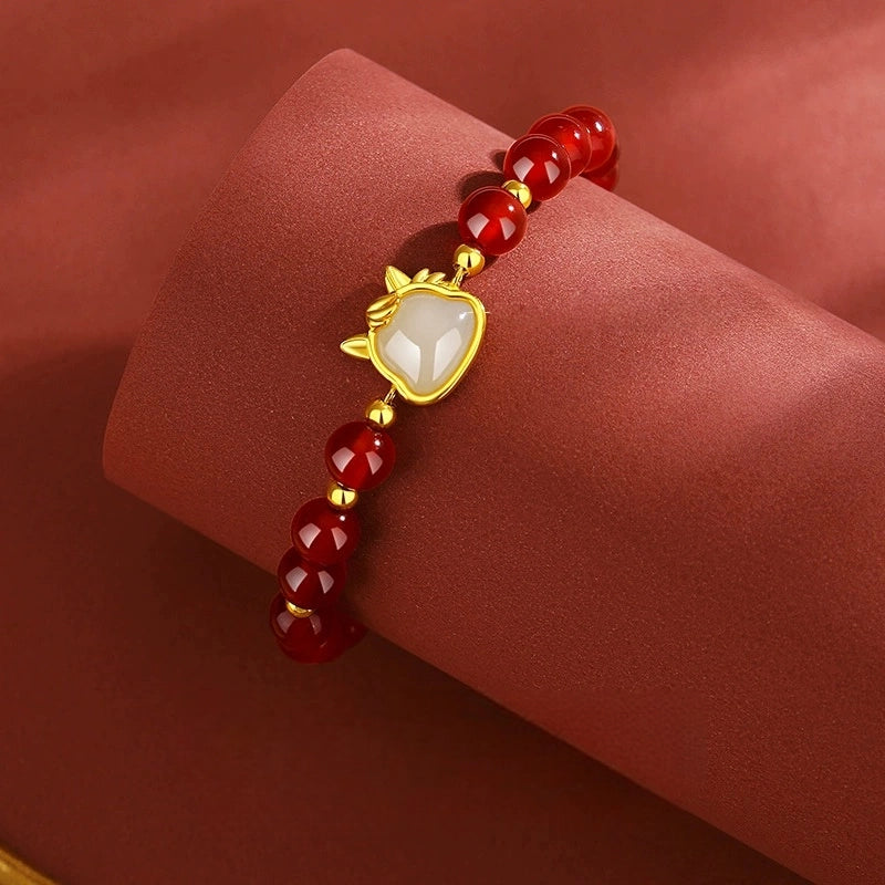 Close-up of red agate bracelet with white jade horse center and gold-tone details.