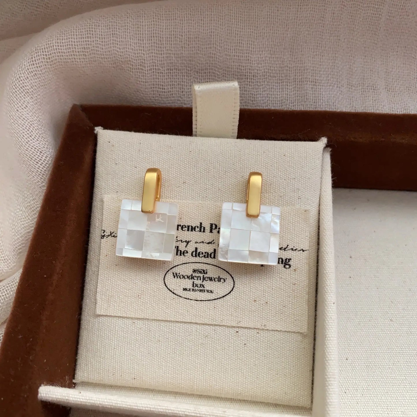 Square mother of pearl checkerboard earrings displayed in a linen jewelry box