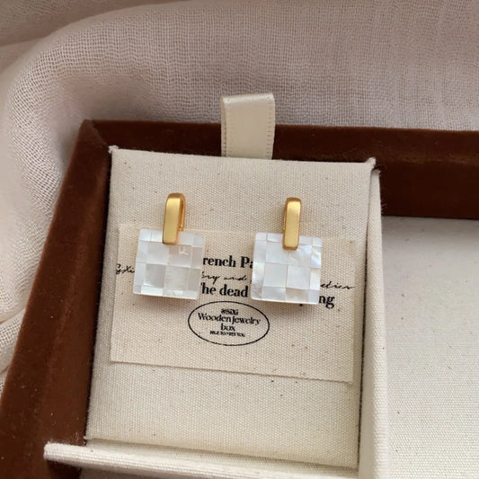 Square mother of pearl checkerboard earrings displayed in a linen jewelry box