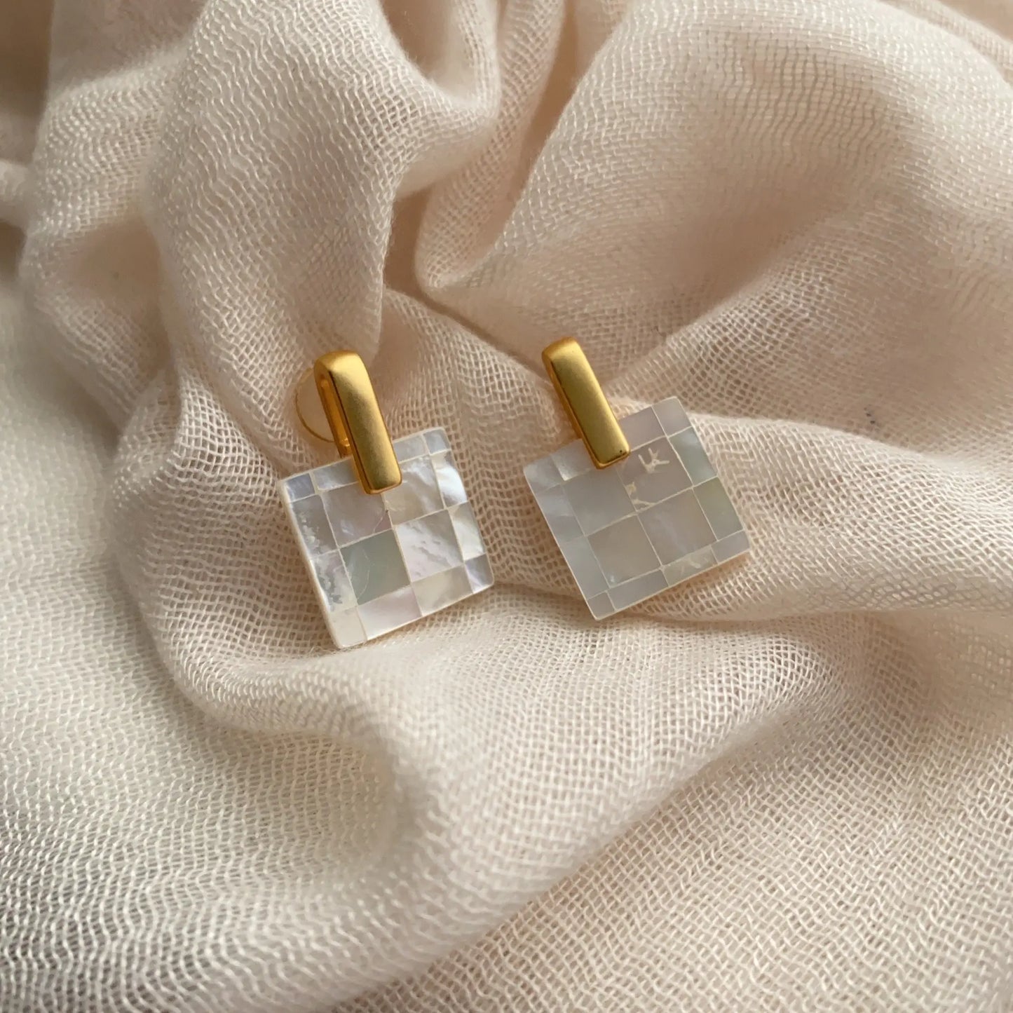 Mother of pearl checkerboard earrings styled on soft neutral fabric