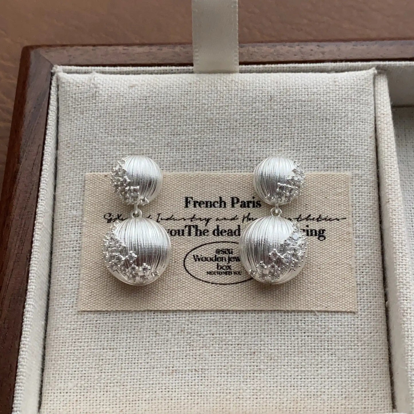 Silver-plated double sphere drop earrings in a minimalist jewelry display