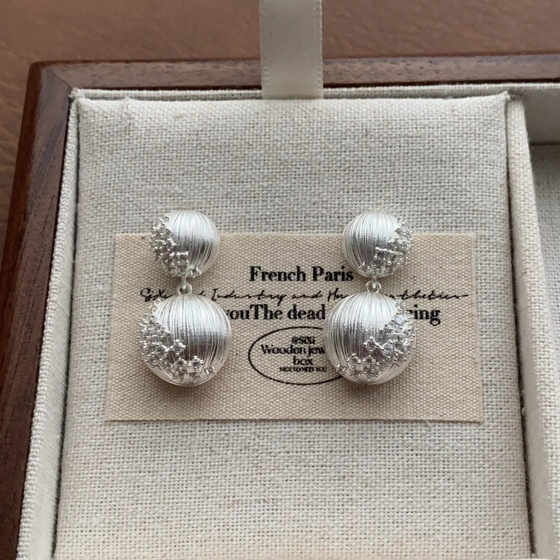 Silver-plated double sphere drop earrings in a minimalist jewelry display