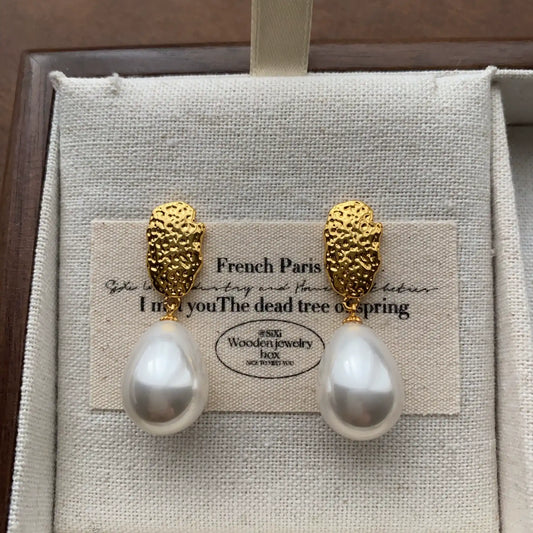 Textured gold teardrop pearl earrings displayed on a cream linen jewelry tray.
