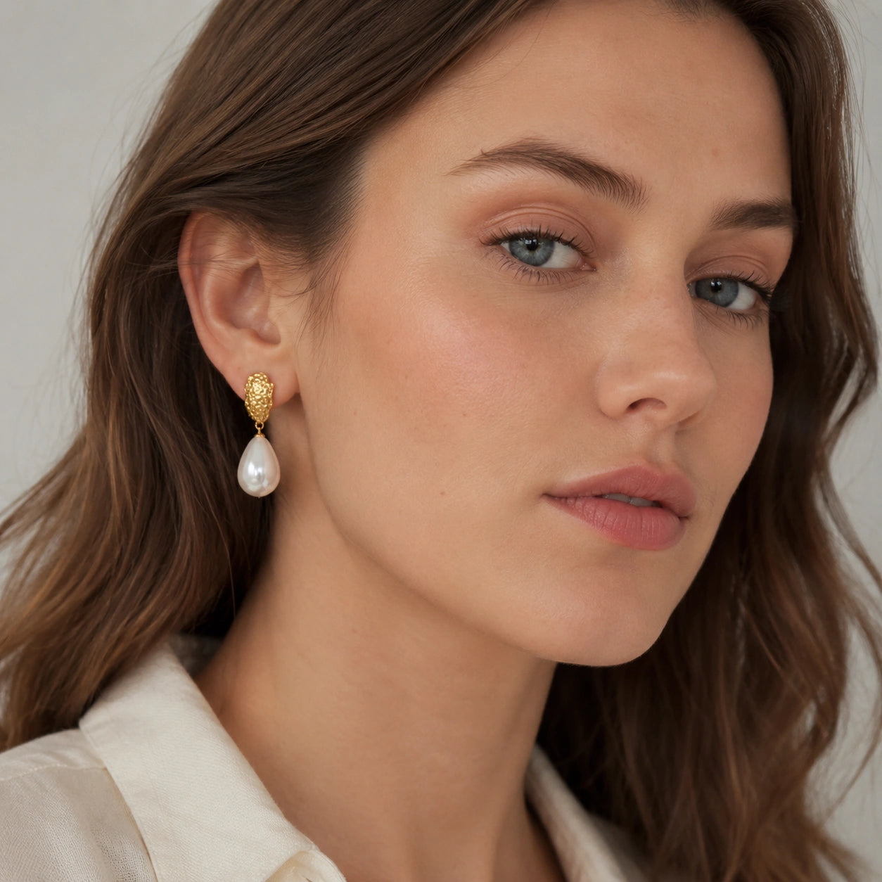 Model wearing textured gold teardrop pearl earrings with a soft neutral blouse.