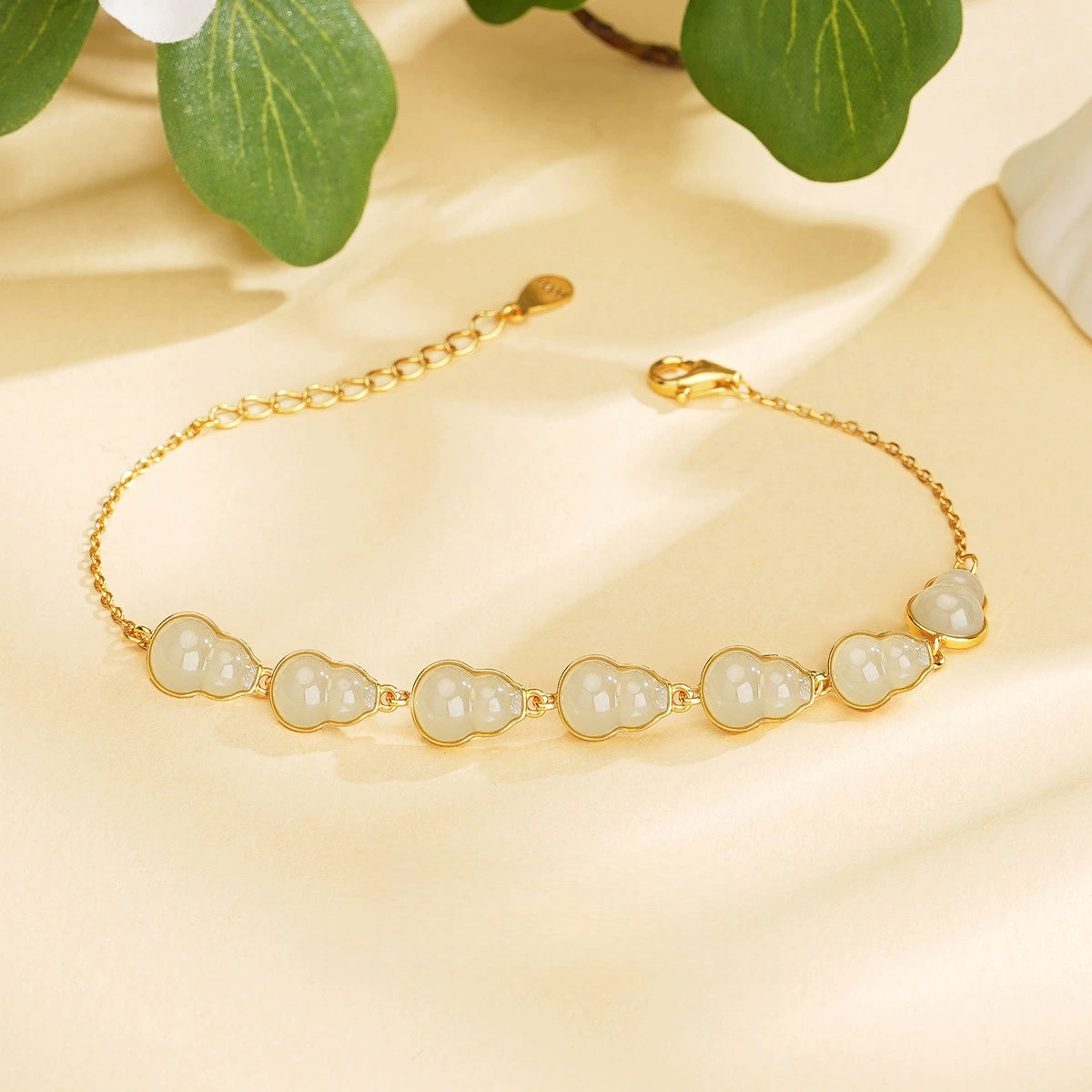 Dainty white Hetian jade hulu bracelet with gold-tone S925 chain on soft satin.